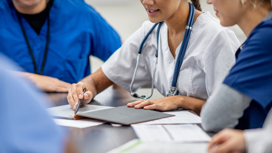Three health care professionals sitting at a table discussing information in a notebook